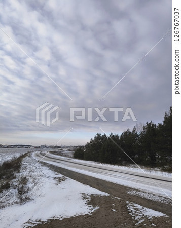 snow-covered rural road on a sharp bend along a field and woodlands. Snowy rural road 126767037