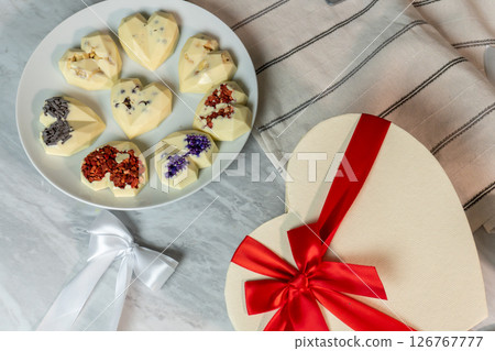 Heart-shaped white chocolates with floral toppings on plate and gift box with red ribbon Heart-shaped white chocolates with floral toppings on plate and gift box with red ribbon 126767777