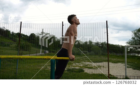 Young sportsman doing push ups on parallel bars at nature. Strong sporty man exercising at sports ground. Male shirtless athlete training hard outdoor. Concept of active sportive lifestyle. Slow mo 126768032