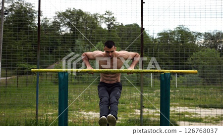 Hardy shirtless sportsman doing exercises on parallel bars at nature. Strong and muscular man working out at sports ground. Young athletic guy exercising outdoor. Concept of active healthy lifestyle Hardy shirtless sportsman doing exercises on parallel bars at nature. Strong and muscular man working out at sports ground. Young athletic guy exercising outdoor. Concept of active healthy lifestyle 126768037