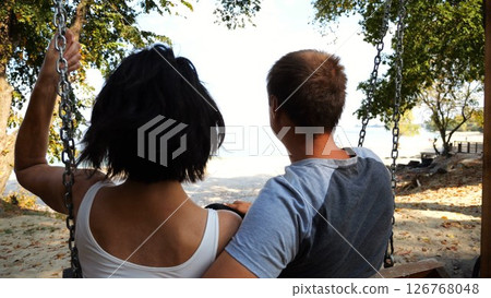 Romantic couple ride on swing together at sea beach. Happy lovers enjoy to spending time together at resort. Carefree pair enjoying rest near ocean at sunny day. Concept of summer vacation or holiday Romantic couple ride on swing together at sea beach. Happy lovers enjoy to spending time together at resort. Carefree pair enjoying rest near ocean at sunny day. Concept of summer vacation or holiday 126768048