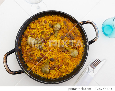 Delicious paella with meats and artichokes in traditional paellera 126768483