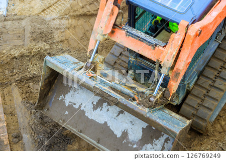 Tractor equipment operates on construction site, moving piles of dirt during works daylight hours 126769249