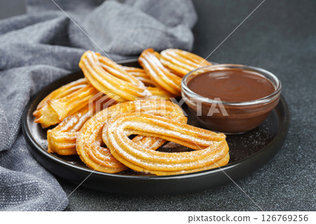 Traditional spanish dessert churros, fried dough pastry and chocolate sause on black background Traditional spanish dessert churros, fried dough pastry and chocolate sause on black background 126769256