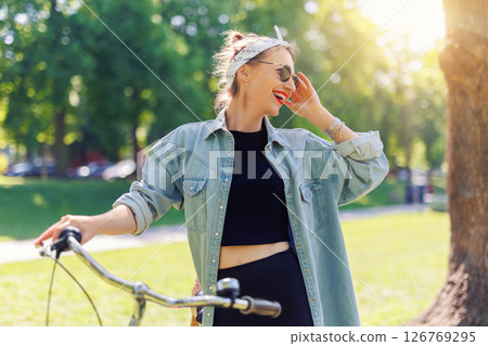 Portrait young adult pretty woman with red vintage retro bike and pin-up casual outfit green city park bright sunny summer day. Happy beautiful female person cycling outdoors. Healthy lifestyle 126769295