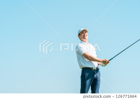 Male golfer swinging a driver at a golf course (blue sky) Male golfer swinging a driver at a golf course (blue sky) 126771664