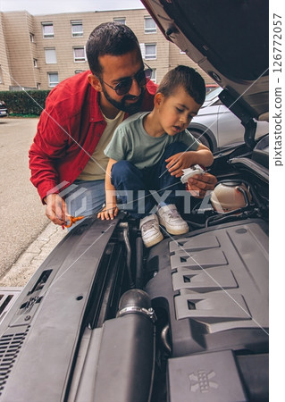 Father and sons repairing car together with the hood open. A heartfelt moment of bonding, fatherhood, parenting, teamwork, and learning. Celebrating Father Day through shared hands-on experience. 126772057