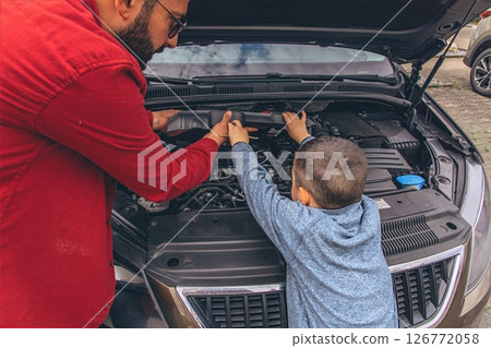 Father and sons repairing car together with the hood open. A heartfelt moment of bonding, fatherhood, parenting, teamwork, and learning. Celebrating Father Day through shared hands-on experience. 126772058