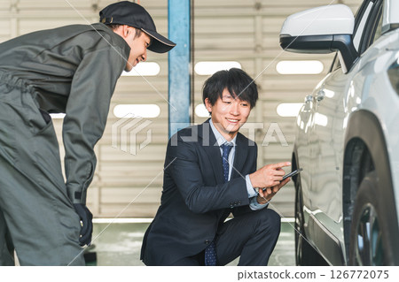 A male mechanic and a salesman in a suit checking scratches and dents on a car 126772075
