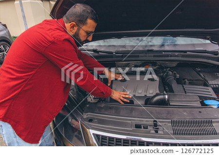 A man repairing his car with the hood open, focused on the engine. Concept of maintenance, auto repair, responsibility, and hands-on work. Everyday moment of problem-solving and care for his vehicle A man repairing his car with the hood open, focused on the engine. Concept of maintenance, auto repair, responsibility, and hands-on work. Everyday moment of problem-solving and care for his vehicle 126772125