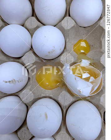 spoiled and cracked low-quality eggs arranged in carton showing signs decay and mishandling. closeup 126772847