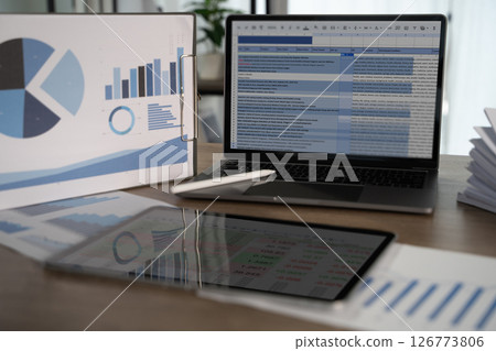 Report file modern workspace with laptop displaying spreadsheet, tablet showing data, and presentation board with charts, indicating business Report file modern workspace with laptop displaying spreadsheet, tablet showing data, and presentation board with charts, indicating business 126773806