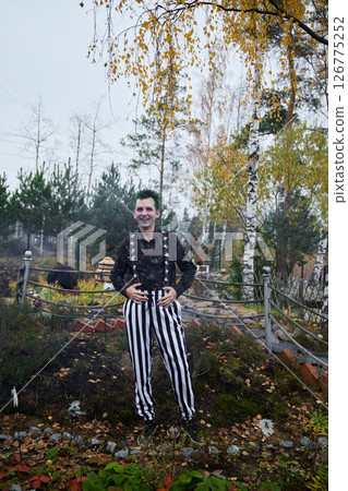 A Mysterious Clown in Colorful Striped Pants Stands Amid Beautiful Autumn Scenery 126775252