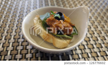 Gourmet Bruschetta Appetizer with Tomato Sauce Spinach and Black Olive on Bread Slice in White Ceramic Dish on Woven Table Mat 126776602