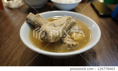 Steaming Bowl of Pork Rib Soup with Garlic and Light Broth Served in a White Ceramic Bowl on a Wooden Table in a Casual Dining Setting with a Blurred Background Steaming Bowl of Pork Rib Soup with Garlic and Light Broth Served in a White Ceramic Bowl on a Wooden Table in a Casual Dining Setting with a Blurred Background 126776665