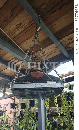 Hanging industrial lamp made from recycled TV parts and metal chains under a rustic wooden ceiling with green plants in the background. 126776678