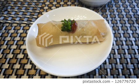 Crispy Spring Roll Garnished with Parsley and Chili Sauce on White Plate with Woven Table Mat Background Crispy Spring Roll Garnished with Parsley and Chili Sauce on White Plate with Woven Table Mat Background 126776720