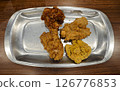 Close-up of assorted fried chicken with four flavors served on a shiny silver plate on a wooden table in a casual dining setting 126776853