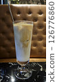 Refreshing iced latte in a tall glass served on a black marble table with a brown tufted leather background in a cozy cafe setting 126776860