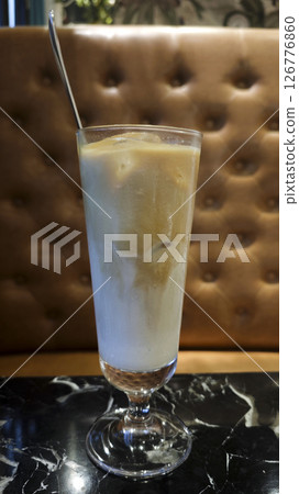 Refreshing iced latte in a tall glass served on a black marble table with a brown tufted leather background in a cozy cafe setting 126776860