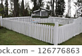 White wooden fence surrounding an outdoor rabbit shelter with greenery and tall trees in a peaceful countryside garden setting 126776863