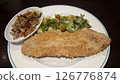 Crispy breaded fish fillet served with sauteed chili onions roasted potatoes fresh green salad and parsley garnish on a white plate creating a vibrant and appetizing dish presentation. 126776874