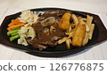Grilled beef steak served with creamy brown gravy crispy potato wedges french fries and sauteed vegetables on a black sizzling plate creating a delicious hearty meal presentation. 126776875