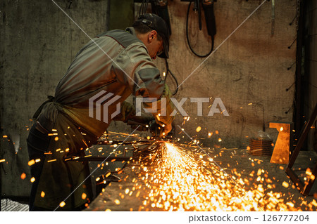 Industrial Metalworker Using Angle Grinder in Workshop with Flying Sparks 126777204