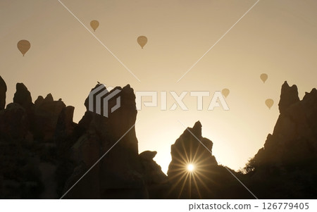 The bright sun breaks through the rocky peaks in Cappadocia, Turkey. Hot air balloons. Background. Beautiful sunrise. Travel Tour. Turkish culture, Goreme. Adventure. Inspiration. Admiration. Geology 126779405