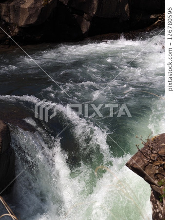 A clear stream flowing powerfully between the rocks 126780596