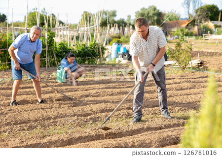 Man tilling ground in garden with mature parents 126781016