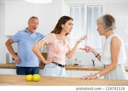 Quarrel between an elderly mother and an adult daughter in home kitchen. Father tries to calm everyone Quarrel between an elderly mother and an adult daughter in home kitchen. Father tries to calm everyone 126781126