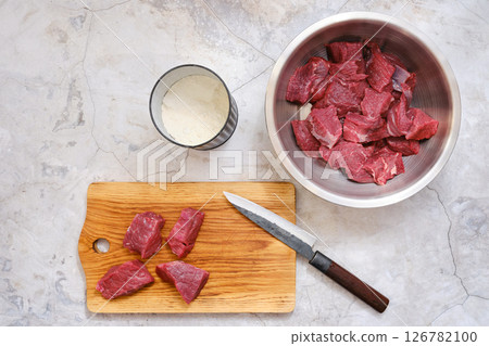 Freshly cut beef chunks prepared for cooking on a wooden board with utensils and ingredients nearby 126782100
