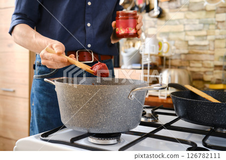 A person adding a rich tomato paste to a pot in a kitchen setting 126782111
