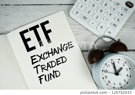 ETF Exchange Traded Fund text on paper notebook page with alarm clock and calculator on wooden background 126782635