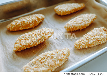 Raw frozen breaded chicken pieces on a baking sheet. Raw frozen breaded chicken pieces on a baking sheet. 126783356