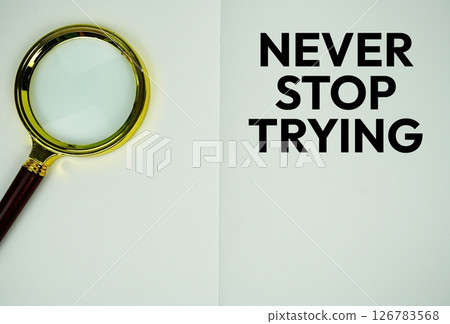 Never Stop Trying text with magnifying glass flat lay on notepad background Never Stop Trying text with magnifying glass flat lay on notepad background 126783568