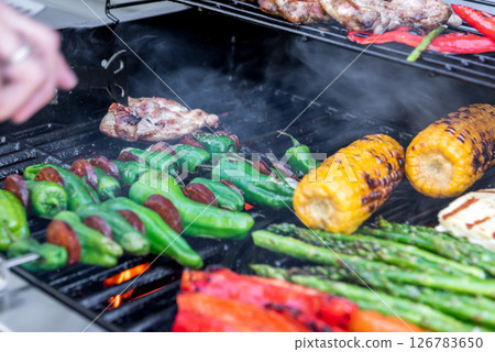 Grilling chicken, corn cobs, paprika, padron, asparagus with temperature control. Meat tongs in human hands. Grilling chicken, corn cobs, paprika, padron, asparagus with temperature control. Meat tongs in human hands. 126783650