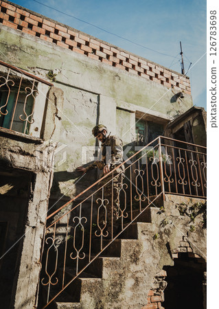 Young Soldier Carefully Goes Down The Stairs Of A Destroyed House Young Soldier Carefully Goes Down The Stairs Of A Destroyed House 126783698