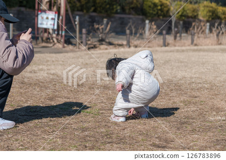 [A one-year-old child and his mother playing on the grass at Sagamihara Municipal Asamizo Park, using a smartphone] 126783896