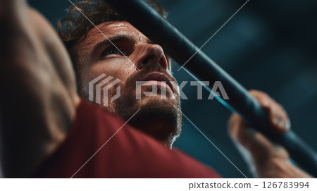 Focused man engages in intense pull-ups at a bustling gym 126783994