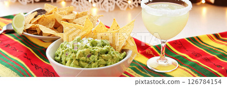 Cinco de Mayo table with guacamole, tortilla chips, festive drink in vibrant setting 126784154