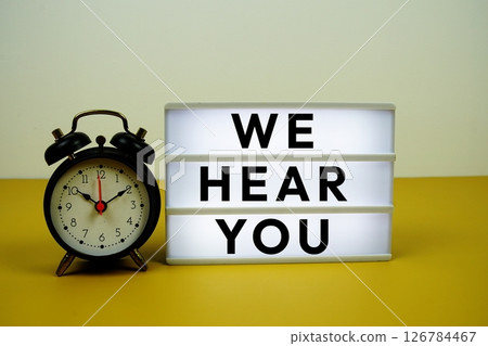 We Hear You text on LED lightbox with alarm clock on yellow background 126784467