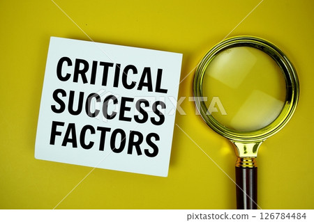 Critical Success Factors text on paper card with magnifying glass flat lay on yellow background 126784484