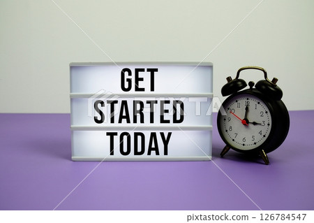 Get Started Today text on LED lightbox with alarm clock on purple background Get Started Today text on LED lightbox with alarm clock on purple background 126784547