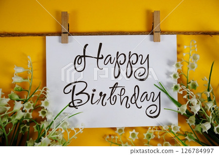 Happy Birthday text on paper card with flower blooming decoration on yellow background Happy Birthday text on paper card with flower blooming decoration on yellow background 126784997