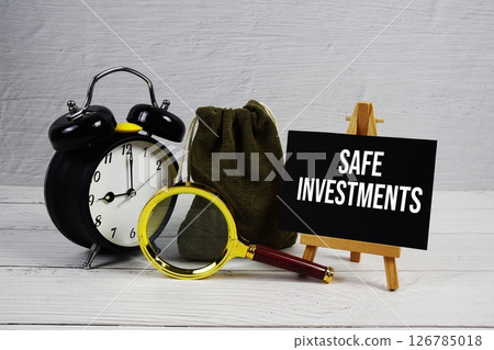 Safe Investments text with alarm clock and magnifying glass on wooden background 126785018