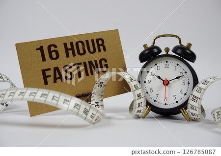 16 Hour Fasting text with alarm clock and measure tape on white background 16 Hour Fasting text with alarm clock and measure tape on white background 126785087
