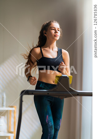 Young woman running on a treadmill indoors Young woman running on a treadmill indoors 126785836