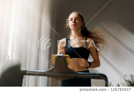 Young woman running on a treadmill indoors Young woman running on a treadmill indoors 126785837